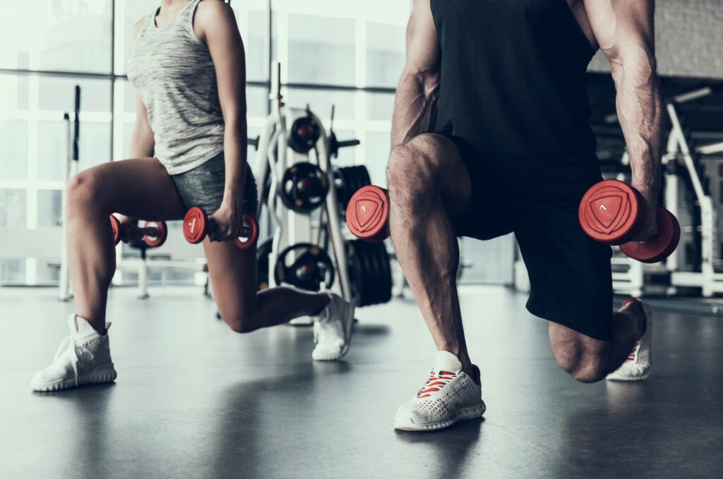 Two people performing lunges in the gym with weights