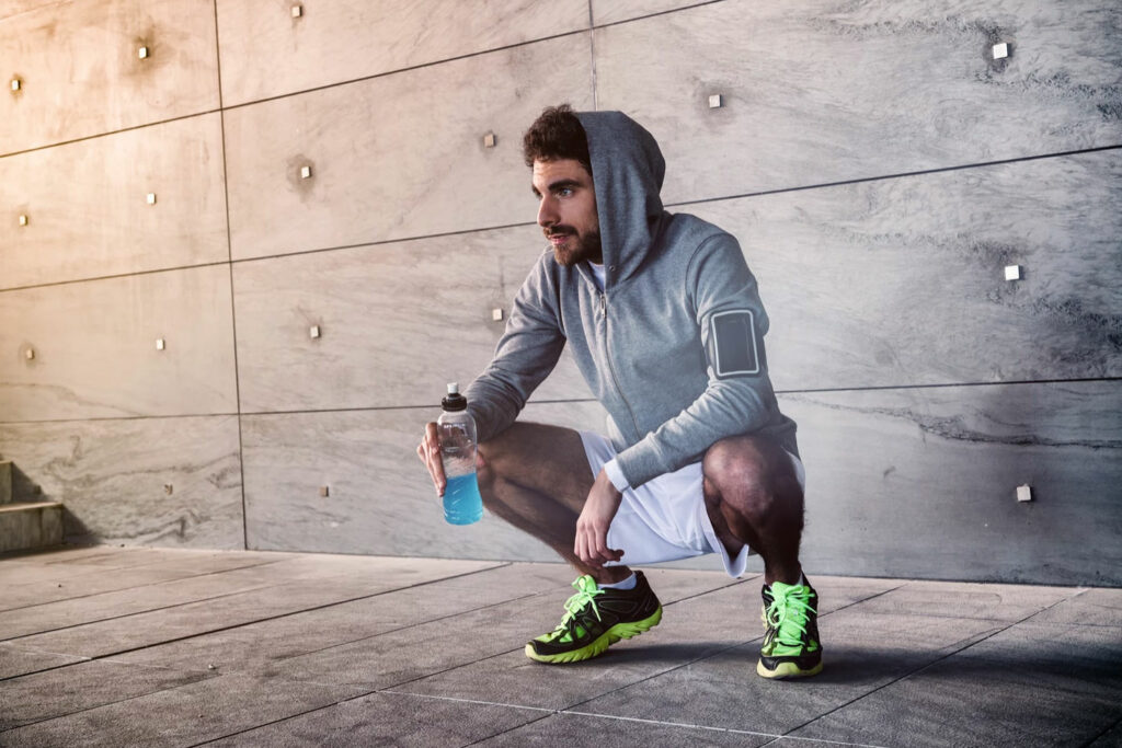 man-in-hoddy-squatting-wearing-running-shoes-holding-water-bottle